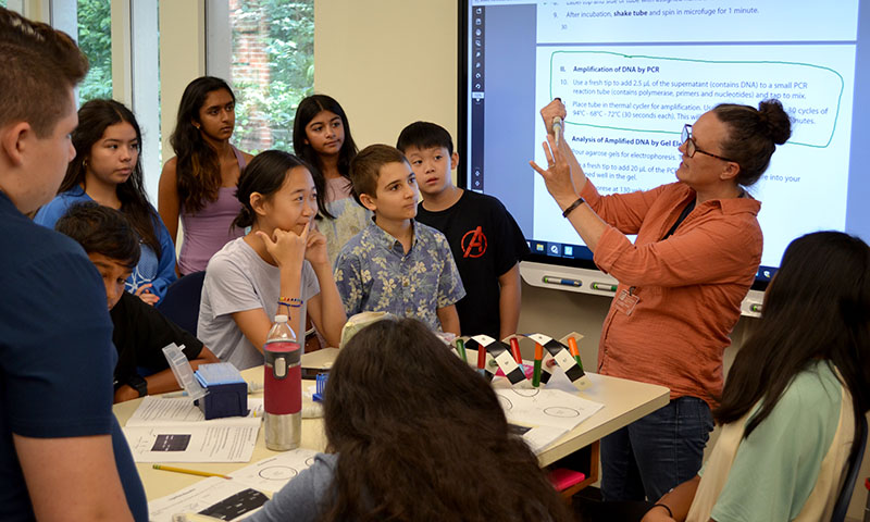 Educator demonstrating lab technique to students gathered around a desk